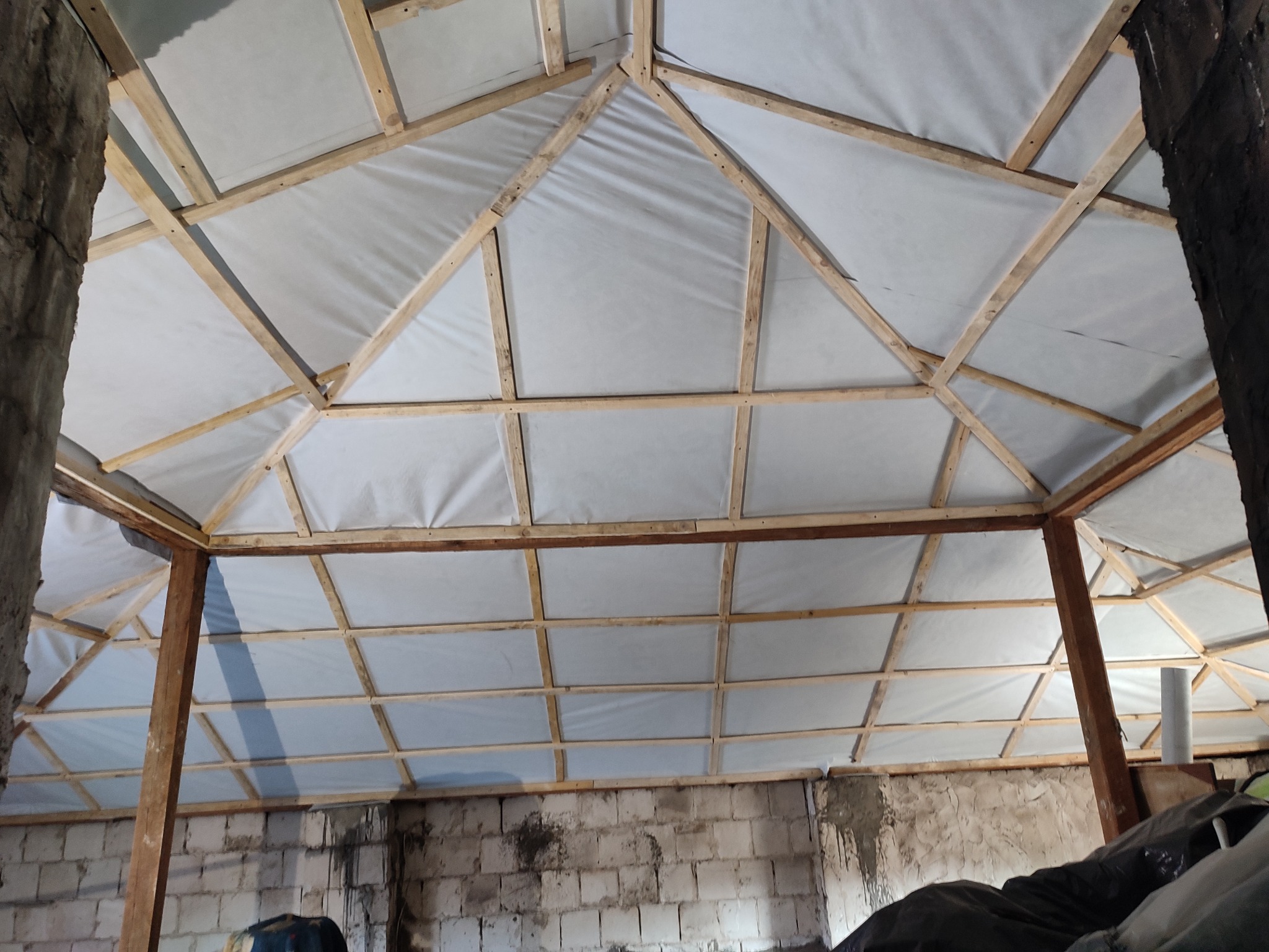 Konstrukcja drewniana poddasza z rozpiętą białą folią, widok od dołu, surowe ściany z pustaków.