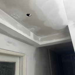 Jan Antoszczyk - Wnętrze w trakcie prac wykończeniowych: sufit z otworem na oświetlenie, ściany pokryte szpachlą, widoczna futryna drzwi. Ujęcie z dołu, ukazujące detale sufitu.