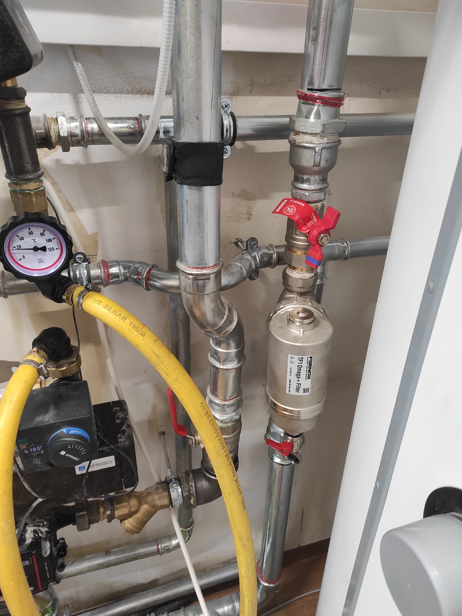Instalacja grzewcza z widocznym manometrem, pompą obiegową Afriso, filtrem Fernox TF1 Omega+ oraz rurami stalowymi z czerwonymi zaworami kulowymi.