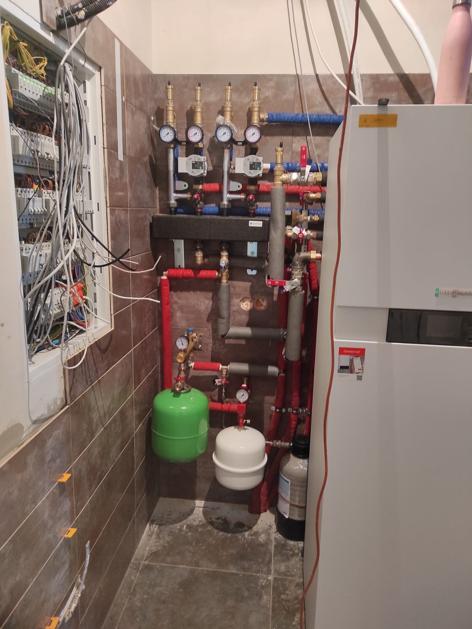 Kompleksowa instalacja CO z piecem Viessmann, widoczne rury, zawory, manometry, zbiorniki wyrównawcze i rozdzielnica elektryczna na brązowej ścianie z płytek.