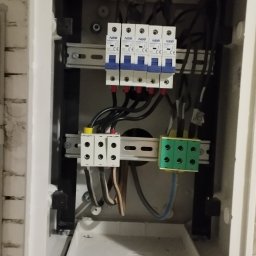 Delta - elektryk Gorzów - Otwarta skrzynka elektryczna z bezpiecznikami NEO, listwami zaciskowymi i przewodami. Widoczne elementy instalacji elektrycznej wewnątrz obudowy.