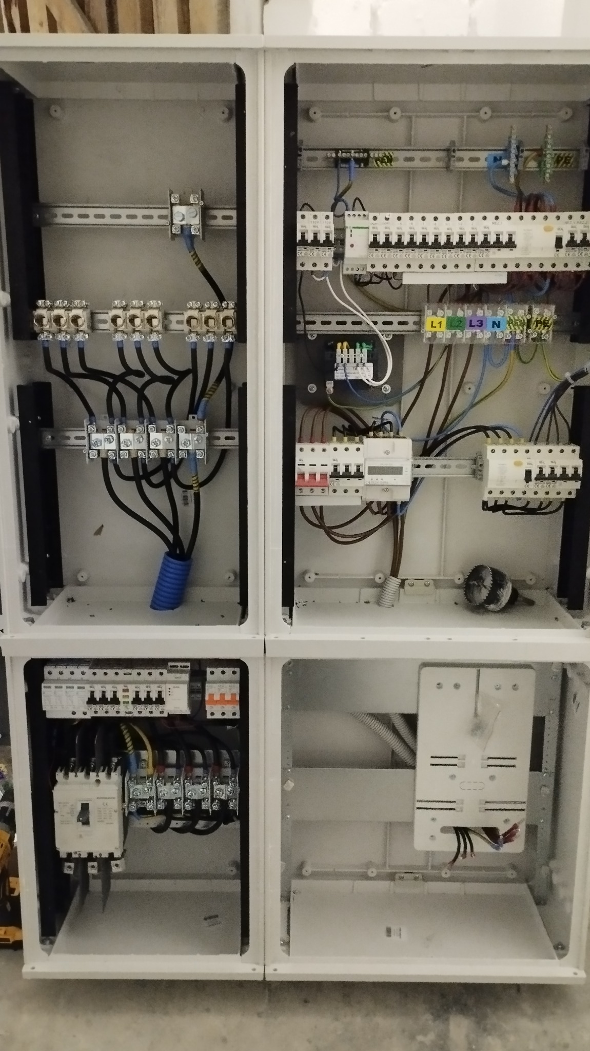 Rozdzielnica elektryczna w trakcie montażu, widoczne zabezpieczenia, przewody w peszlu i inne elementy osprzętu, wnętrze szafy oświetlone, widoczne ślady montażu.