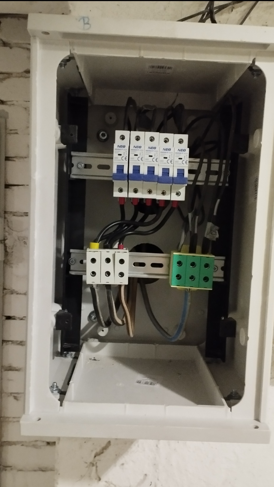 Otwarta skrzynka elektryczna z bezpiecznikami NEO, listwami zaciskowymi i przewodami. Widoczne elementy instalacji elektrycznej wewnątrz obudowy.