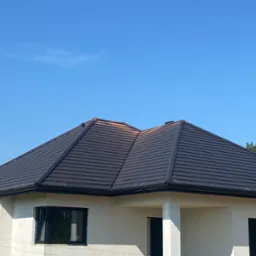 Nowy, ciemny dach z dachówki ceramicznej na jasnym, nieotynkowanym domu jednorodzinnym w słoneczny dzień.