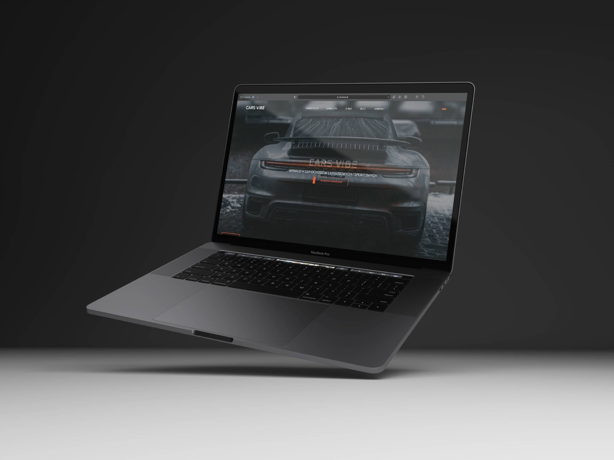 Laptop MacBook Pro wyświetlający stronę internetową Cars Vibe z luksusowym samochodem sportowym na tle deszczowej ulicy, minimalistyczne studio w odcieniach szarości.