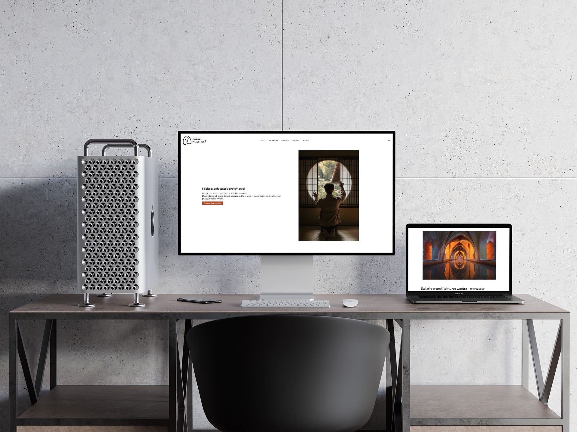 Ekran monitora prezentujący stronę internetową z minimalistycznym designem, obok komputer stacjonarny typu tower i laptop na biurku z metalowymi nogami i betonowym tłem.