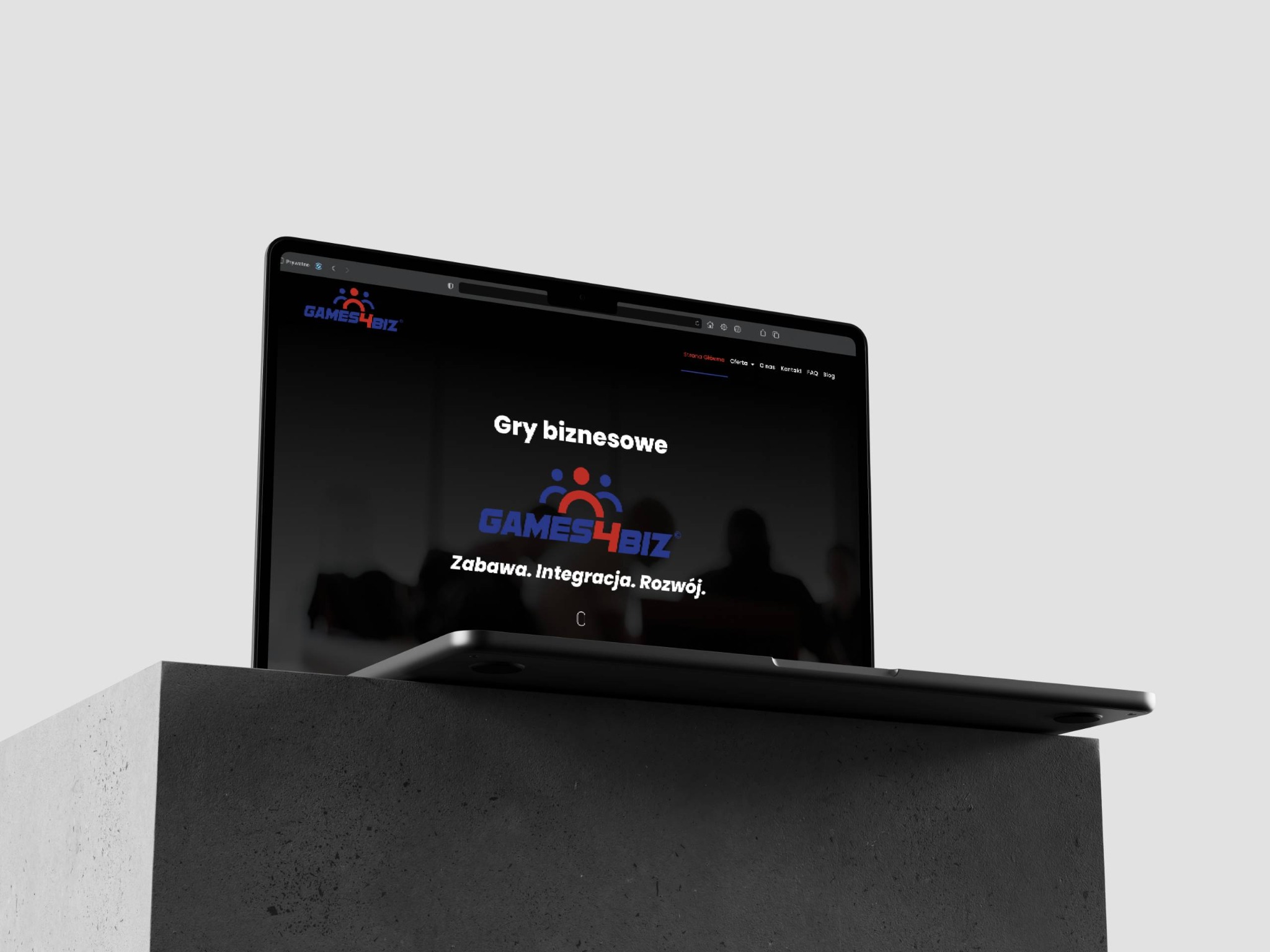 Laptop prezentujący stronę internetową z motywem gier biznesowych, umieszczony na betonowym postumencie.