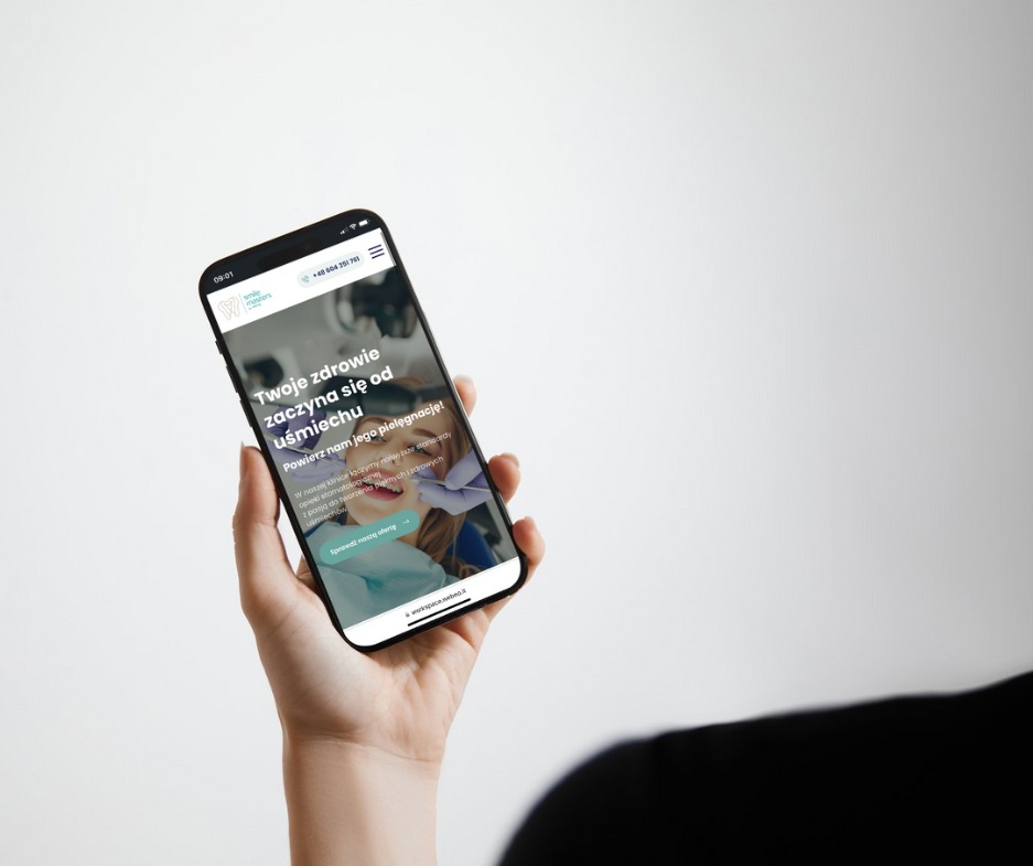 Kobieta trzyma smartfon prezentujący responsywną stronę internetową kliniki dentystycznej z hasłem 'Twoje zdrowie zaczyna się od uśmiechu', na białym tle.
