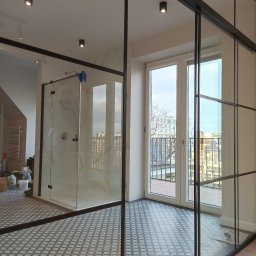 Andrzej Baldin metr.wow.pl - Nowoczesna łazienka z kabiną prysznicową typu walk-in, wykończona marmurową płytką, oddzielona od reszty pomieszczenia szklaną ścianką z czarnymi profilami, widoczne pozostałości po pracach...