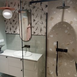 Andrzej Baldin metr.wow.pl - Nowoczesna łazienka z kabiną prysznicową typu walk-in, umywalką nablatową na szafce z szufladami, lustrem w czarnej ramie i tapetą w jaskółki. Na blacie wiertarka.