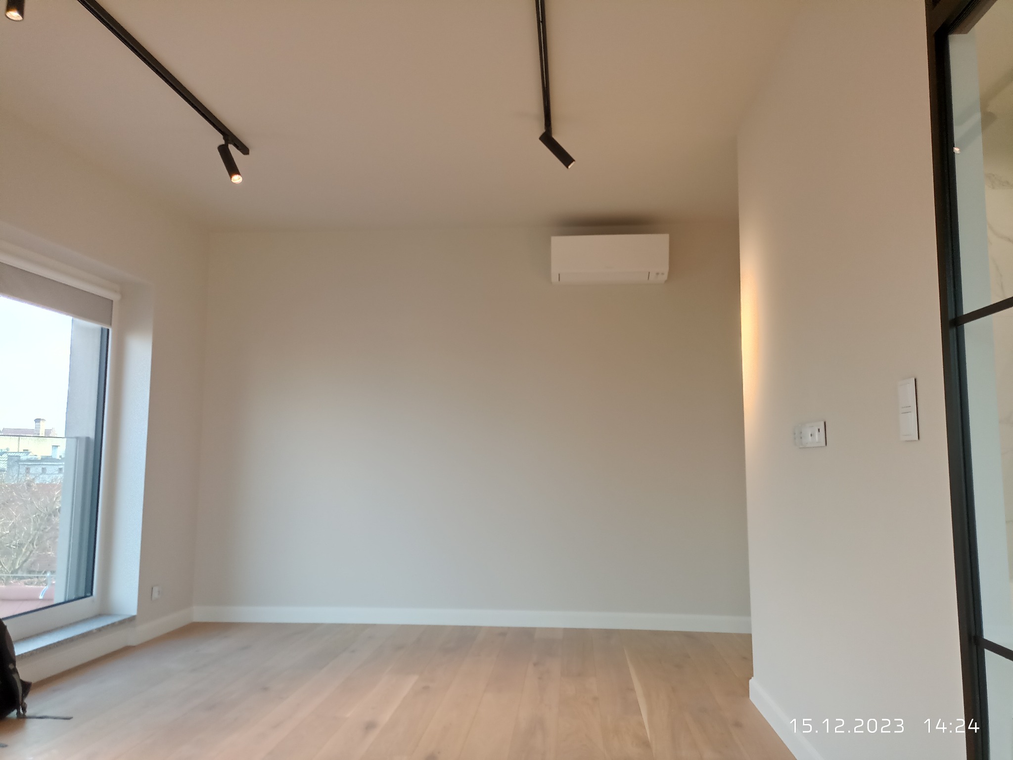 Pusty pokój po remoncie z drewnianą podłogą, świeżo pomalowanymi ścianami w odcieniach beżu, oświetleniem punktowym na szynoprzewodach i klimatyzacją na ścianie.