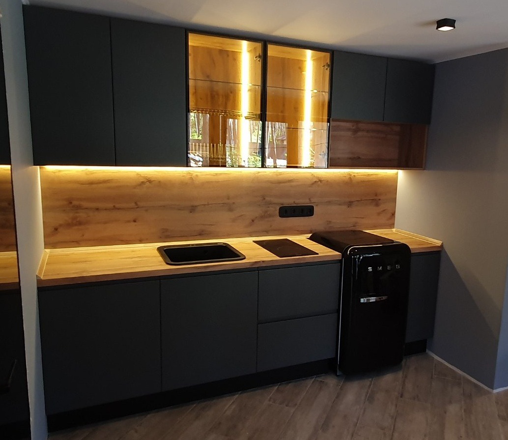 Nowoczesna kuchnia w odcieniach szarości z drewnianym blatem i podświetleniem LED, czarny zlew i płyta indukcyjna, lodówka SMEG w stylu retro.