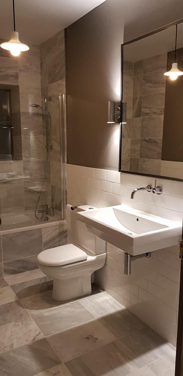 Nowoczesna łazienka z marmurową podłogą i ścianami, wisząca umywalka z baterią, toaleta kompaktowa i kabina prysznicowa za szklaną ścianką.