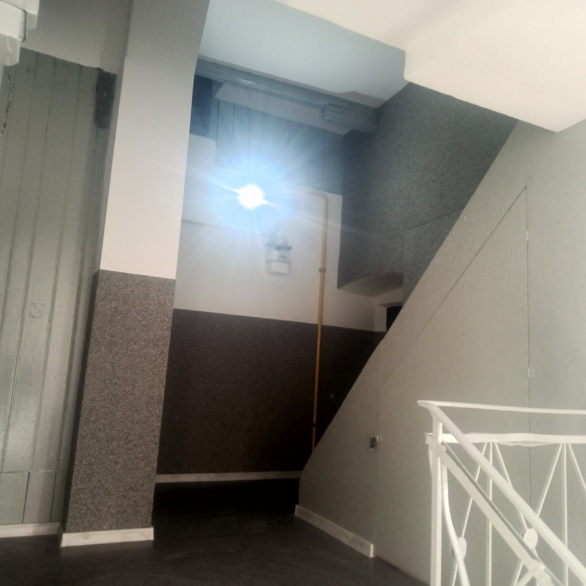 Klatka schodowa po remoncie: szare ściany z ciemniejszym pasem na dole, białe balustrady, kolumna z dekoracyjnym wykończeniem do połowy wysokości. Widok z dołu.