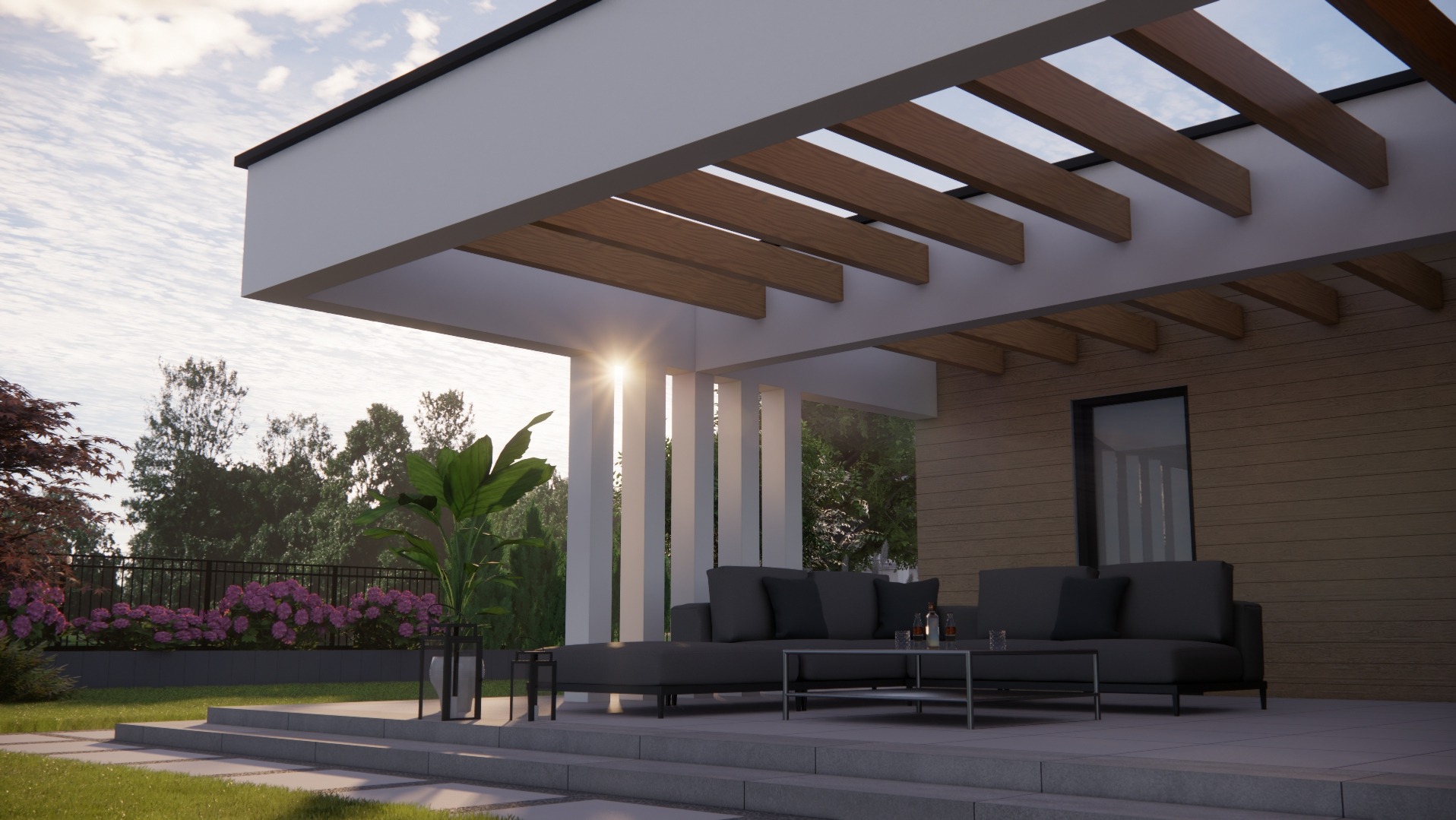 Nowoczesny taras z drewnianą pergolą, szarą sofą i stolikiem kawowym, oświetlony zachodzącym słońcem, z widokiem na ogród z kwitnącymi różowymi krzewami.