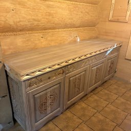 Ufarbiorza - Drewniana komoda z rzeźbieniami w rustykalnym wnętrzu z drewnianych bali. Dekoracyjny element wykończenia i stylizowane płytki podłogowe.