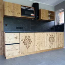 Drewniana kuchnia z frezowanymi wzorami, czarnym blatem i sprzętem AGD. Ujęcie z perspektywy podłogi, ukazujące detale wykończenia i nowoczesny design.