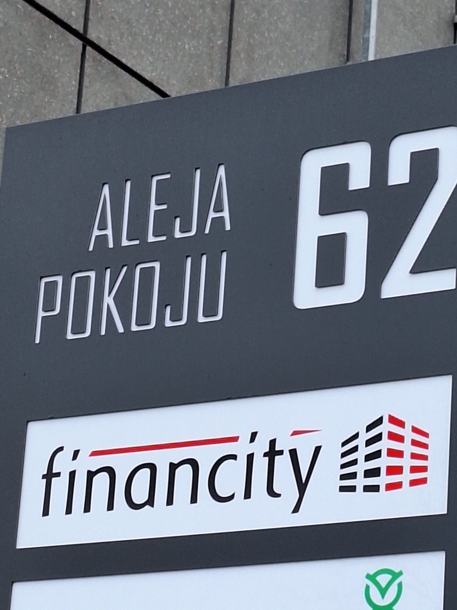 Szyld z adresem Aleja Pokoju 62 i logo firmy Financity z elementami architektonicznymi w kolorach czerni i czerwieni.