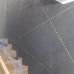 Ściana w odcieniach szarości z dekoracyjnymi, złotymi liniami, częściowo zasłonięta zabezpieczonymi folią schodami.