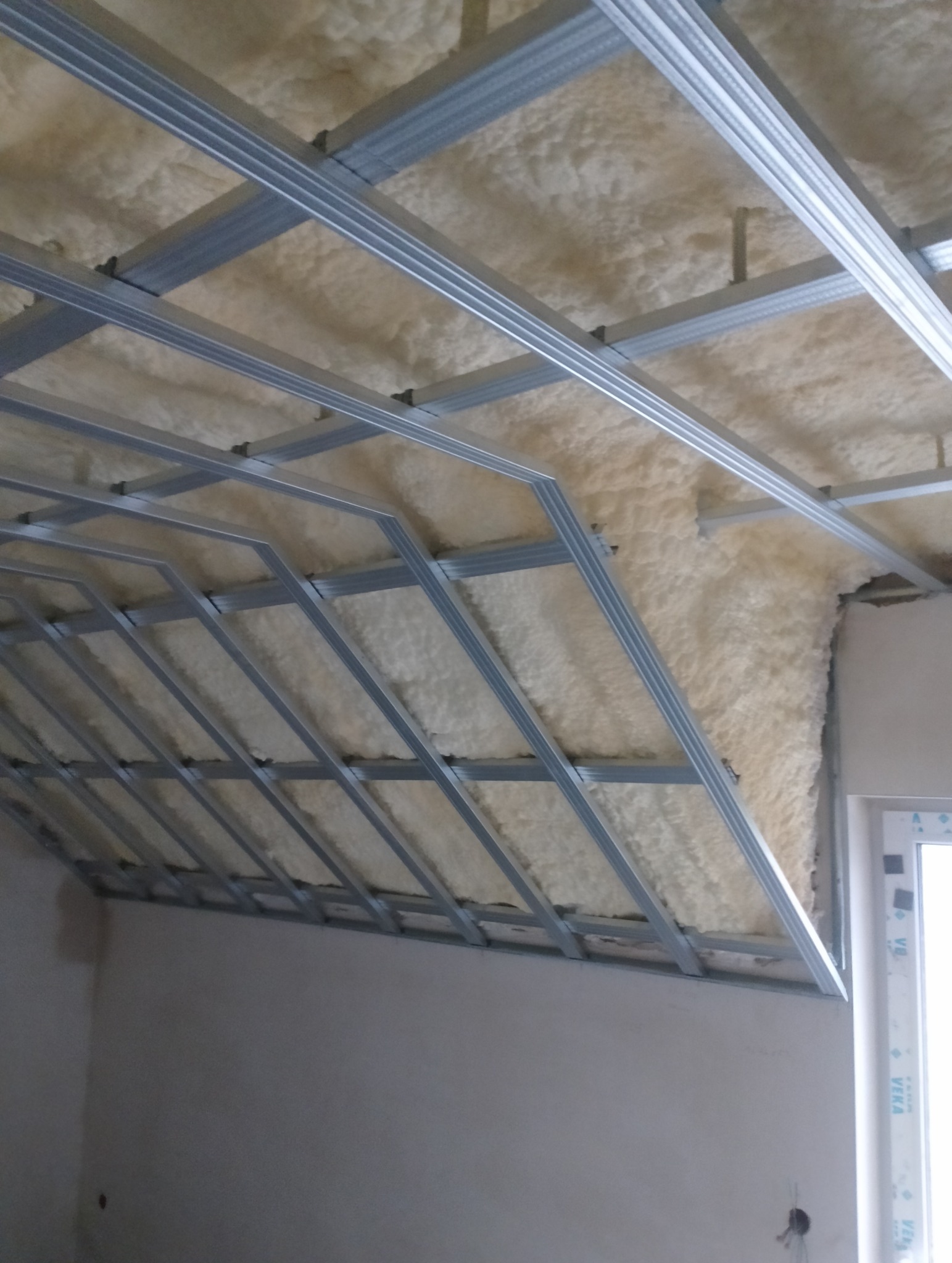 Sufit poddasza z widoczną konstrukcją metalową profili i pianką izolacyjną, przygotowany do dalszych prac wykończeniowych.