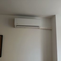 Przemysław Bogdanowicz - Biały klimatyzator marki AUX zamontowany na białej ścianie w pomieszczeniu z oknem i lustrem.