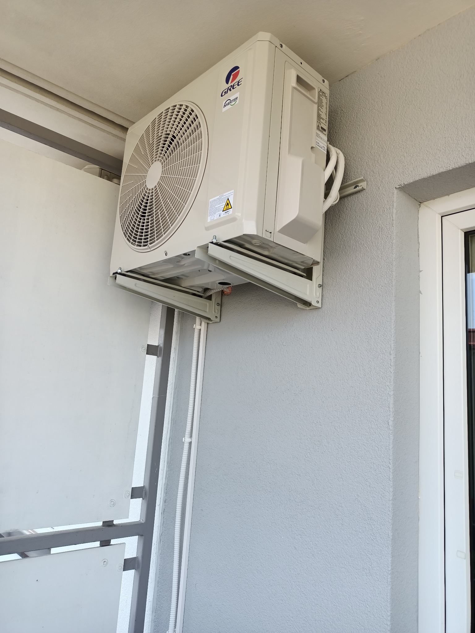 Zewnętrzna jednostka klimatyzacji marki Gree zamontowana na balkonie, widoczne przewody i uchwyty montażowe.