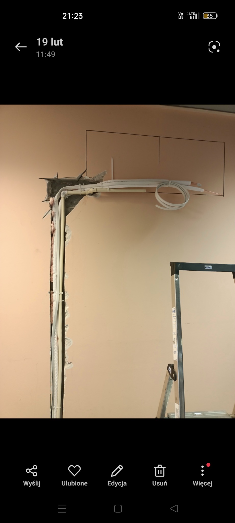 Montaż instalacji freonowej klimatyzacji w ścianie, widoczne rury i przewody w bruździe pod planowanym otworem, drabina w tle.