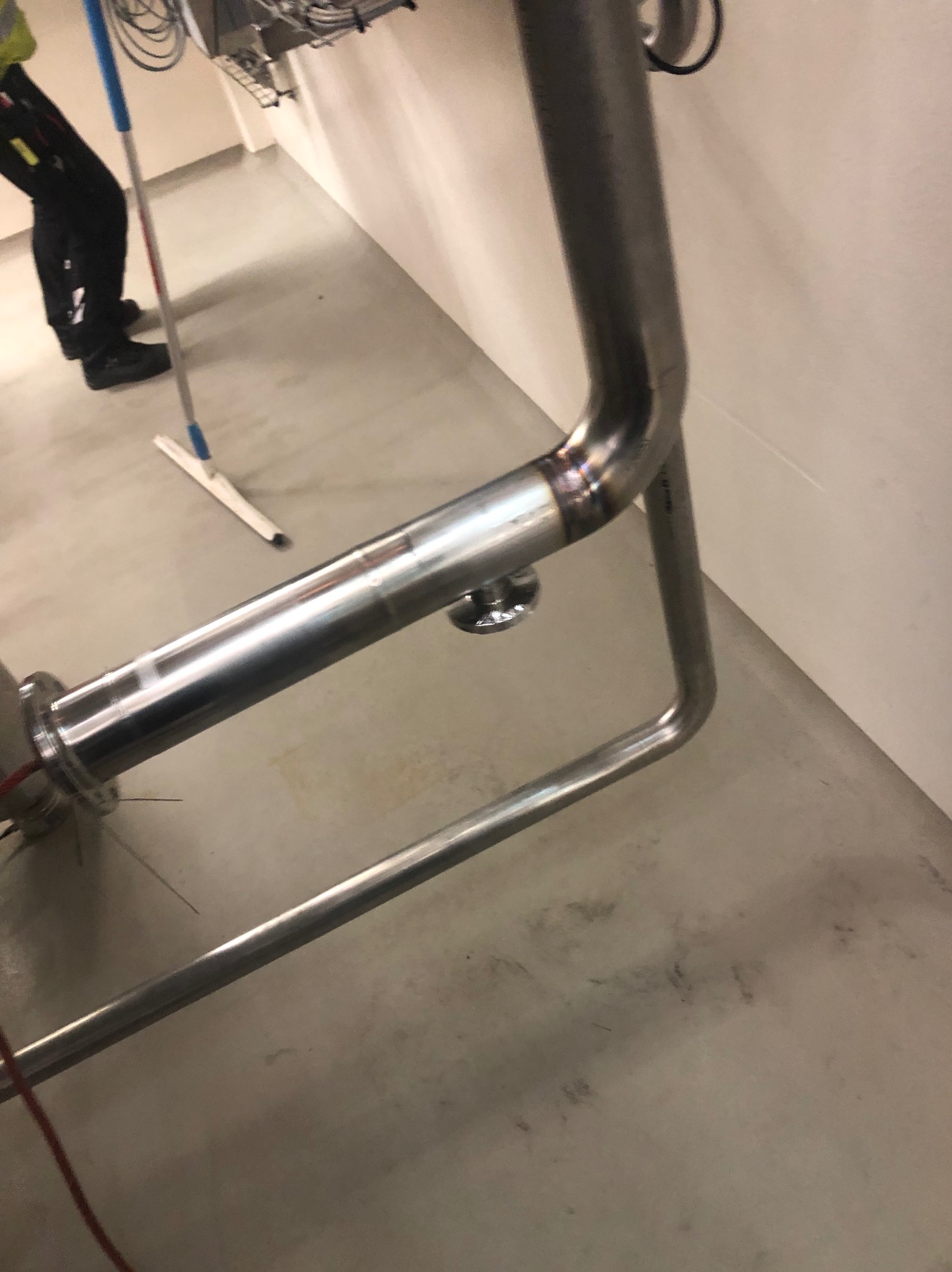 Szczegółowe ujęcie spawu na metalowej konstrukcji rurowej w pomieszczeniu, widoczny spawacz i mop na podłodze.