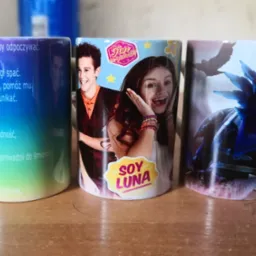 Trzy ceramiczne kubki z różnymi nadrukami: gradientowy z tekstem, z postaciami z serialu 'Soy Luna' i z fantastycznym motywem ptaka i roślin.