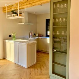 INNOVO MEBLE Magdalena Kłobucka Meble na wymiar - Jasna kuchnia z wyspą i marmurowym blatem, drewniany parkiet w jodełkę, przeszklona witryna z kieliszkami, minimalistyczny design, ciepłe oświetlenie.