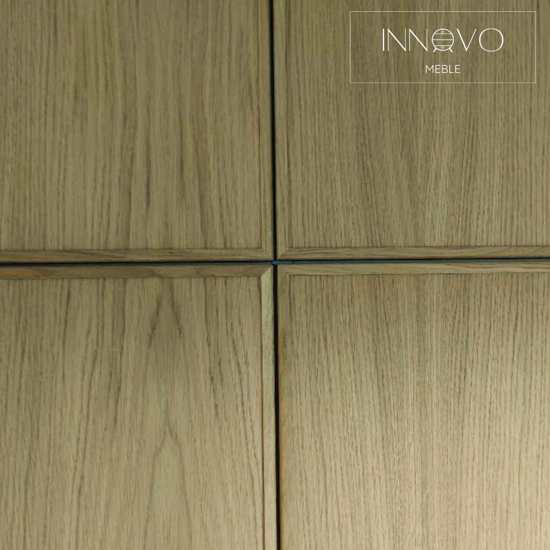 Detale drewnianych frontów szafy z logo 'INNOVO Meble' w prawym górnym rogu. Naturalny odcień drewna, minimalistyczny design.