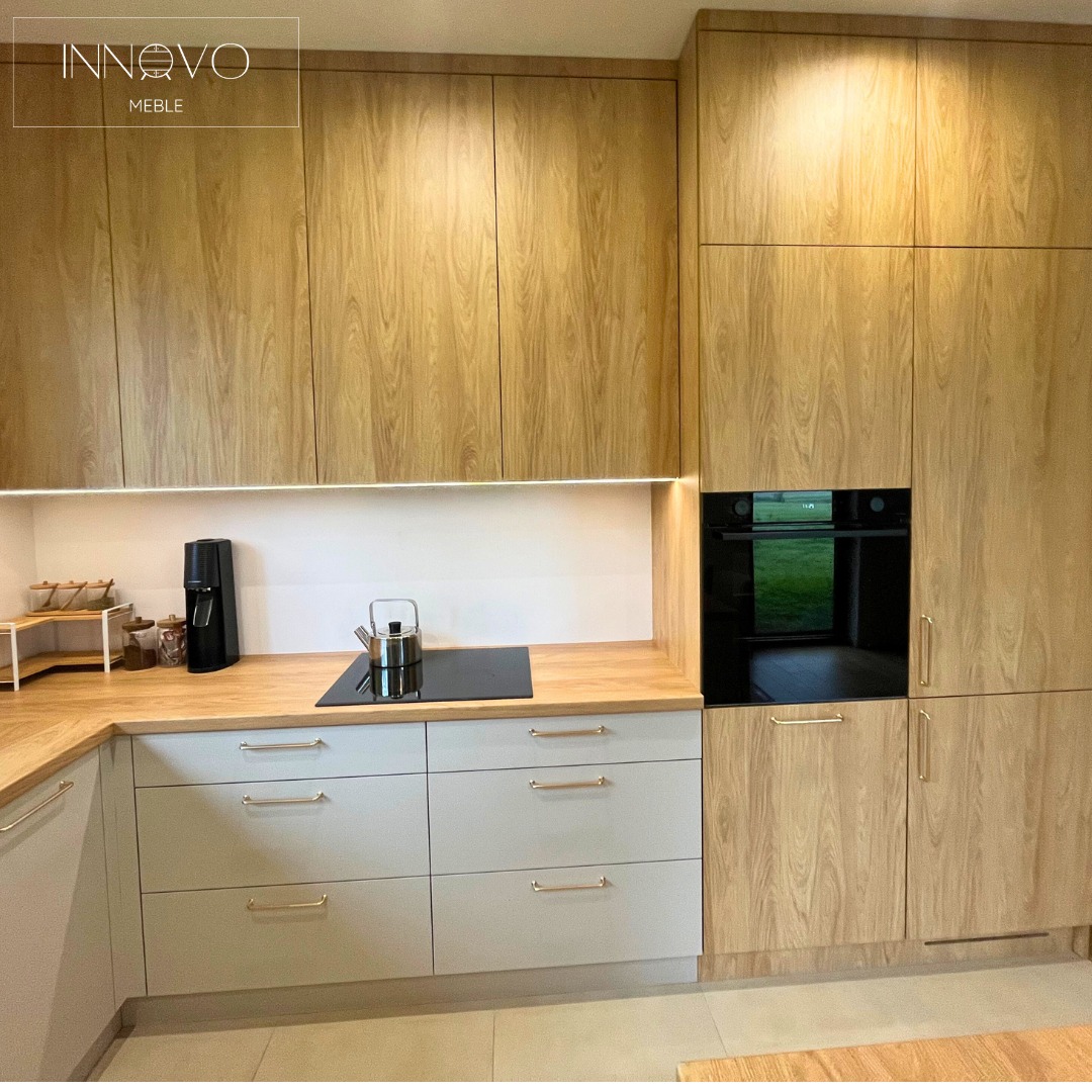 Nowoczesna kuchnia z drewnianymi frontami szafek i szarymi szufladami, oświetleniem LED pod szafkami wiszącymi i wbudowanym piekarnikiem.