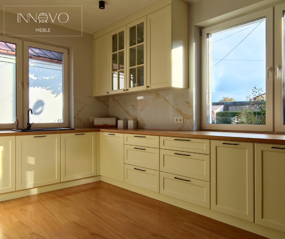 Jasna kuchnia na wymiar z drewnianym blatem i marmurowym backsplashiem, widok z perspektywy podłogi, okno z widokiem na zieleń, czarne detale.