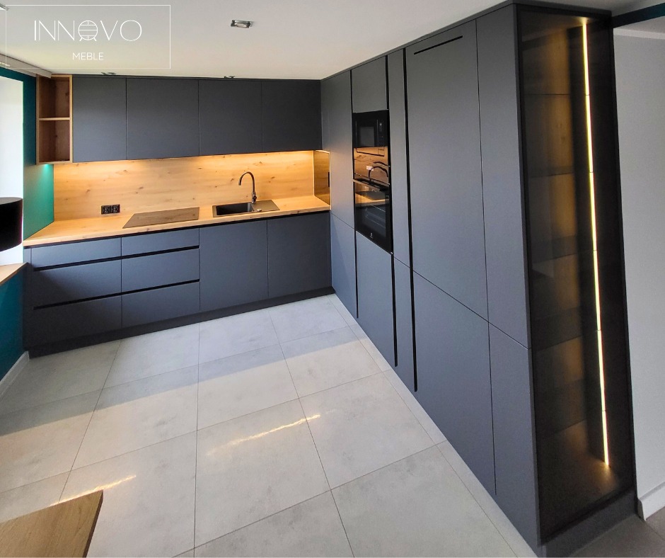 Nowoczesna kuchnia w odcieniach szarości z drewnianym blatem i oświetleniem LED. Minimalistyczny design, zabudowa kuchenna z piekarnikiem i szklaną witryną.