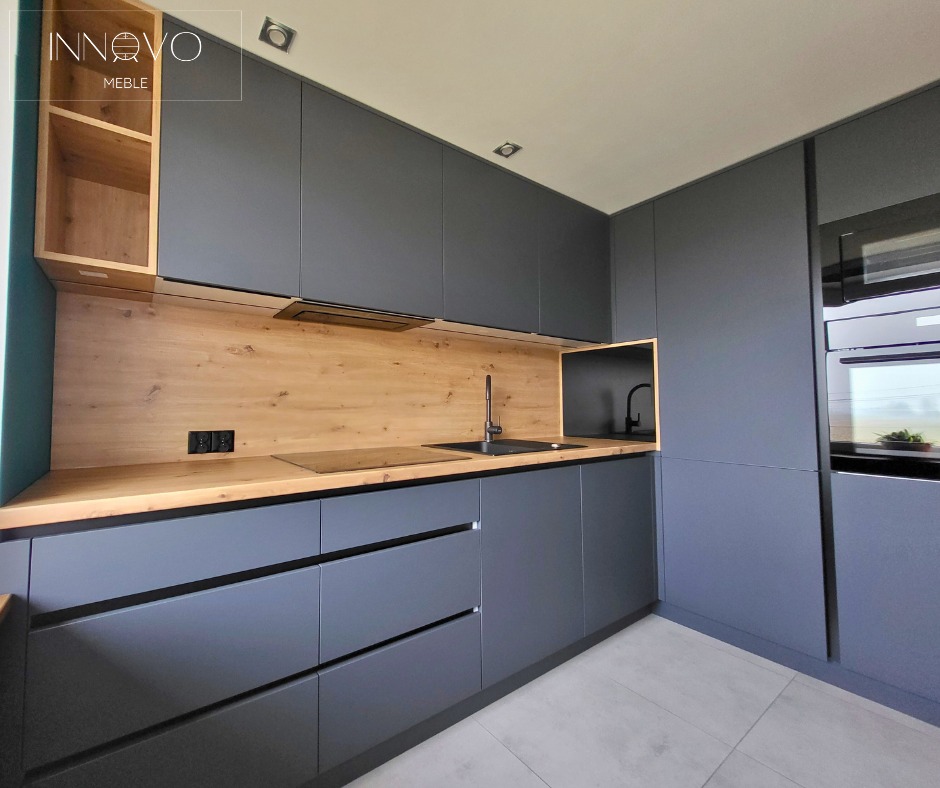 Nowoczesna kuchnia na wymiar w odcieniach szarości z drewnianym blatem i zabudową, czarny zlew i bateria, minimalistyczny design, widok z boku, oświetlenie sufitowe.