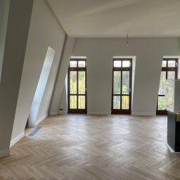 VASBUD - Jasne, przestronne poddasze po remoncie, z parkietem ułożonym w jodełkę, trzema drewnianymi oknami balkonowymi i świeżo pomalowanymi ścianami na neutralny odcień szarości.