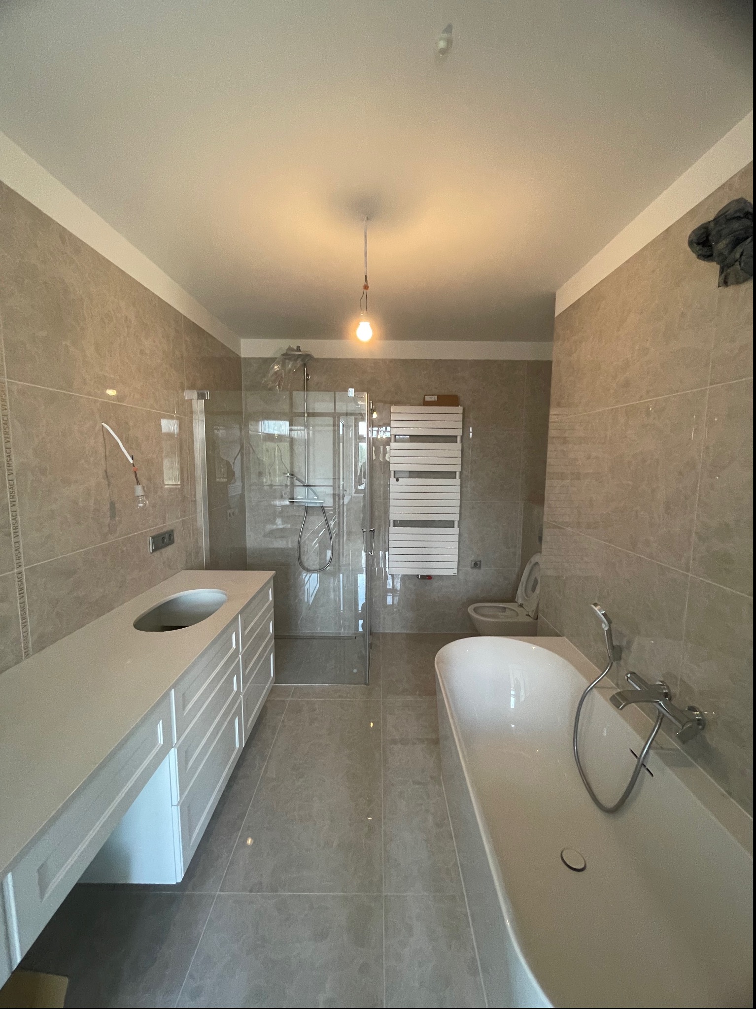 Wykończona łazienka w Warszawie z kabiną prysznicową typu walk-in, białą wanną wolnostojącą i umywalką wpuszczaną w szafkę, wykończona płytkami imitującymi marmur.