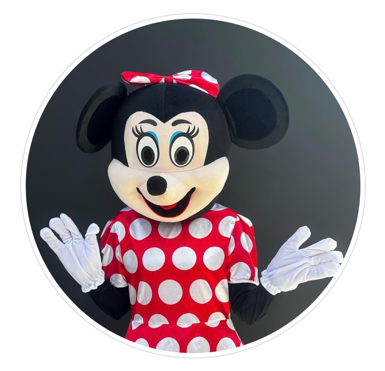 Minnie Mouse w kostiumie, z szeroko rozłożonymi rękami w białych rękawiczkach, na czarnym tle w białym okręgu.