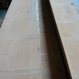 Dwie surowe deski z jasnego drewna z widocznymi słojami i numerami naniesionymi markerem, ułożone obok siebie.