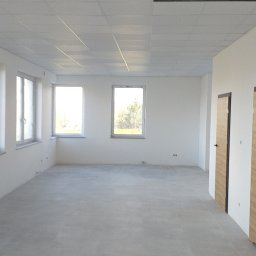 Filmar - Puste, jasne pomieszczenie biurowe z szarą podłogą z płytek, białymi ścianami, trzema oknami i podwieszanym sufitem kasetonowym z widoczną kratką wentylacyjną.