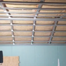 Sufit podwieszany z ociepleniem z wełny mineralnej w trakcie montażu w Pabianicach, widoczne profile metalowe i płyty gipsowo-kartonowe na ścianach.