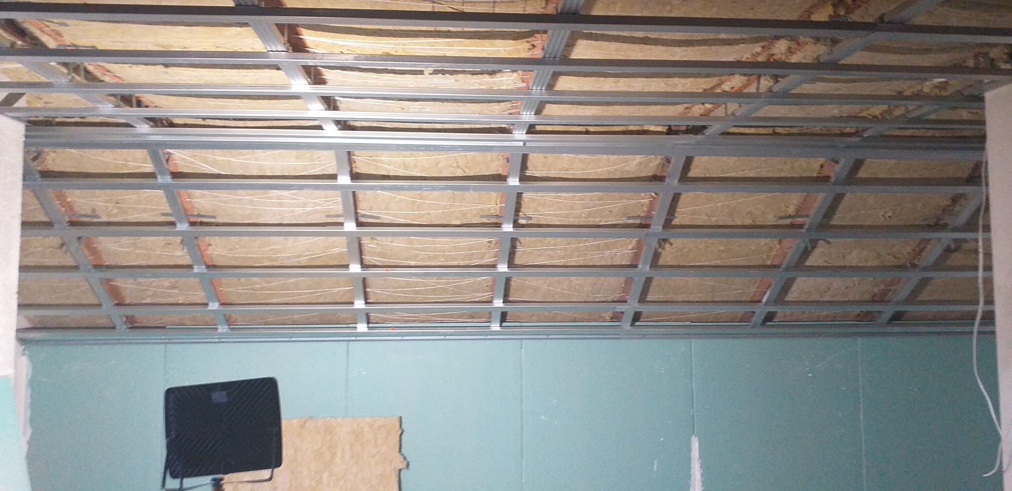 Sufit podwieszany z ociepleniem z wełny mineralnej w trakcie montażu w Pabianicach, widoczne profile metalowe i płyty gipsowo-kartonowe na ścianach.