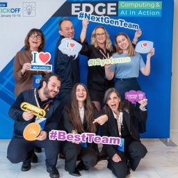 AMT Media - Grupa uśmiechniętych osób pozuje na tle firmowej ścianki reklamowej z hasłami #NextGenTeam, #iSystems, #BestTeam i rekwizytami 'I love my team', 'Hard worker', 'Coffee lover' podczas wydarzenia...