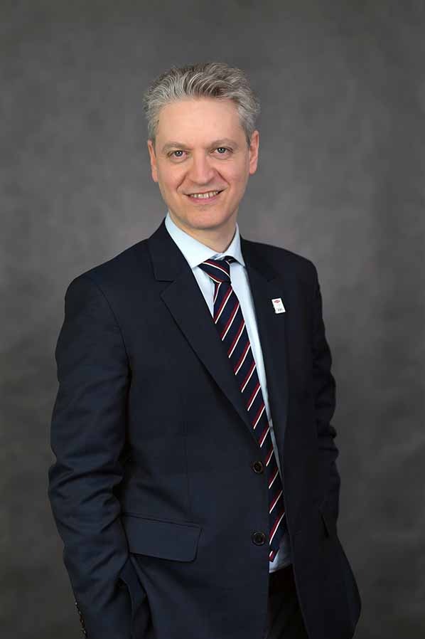 Portret uśmiechniętego mężczyzny w garniturze i krawacie w paski na szarym tle.