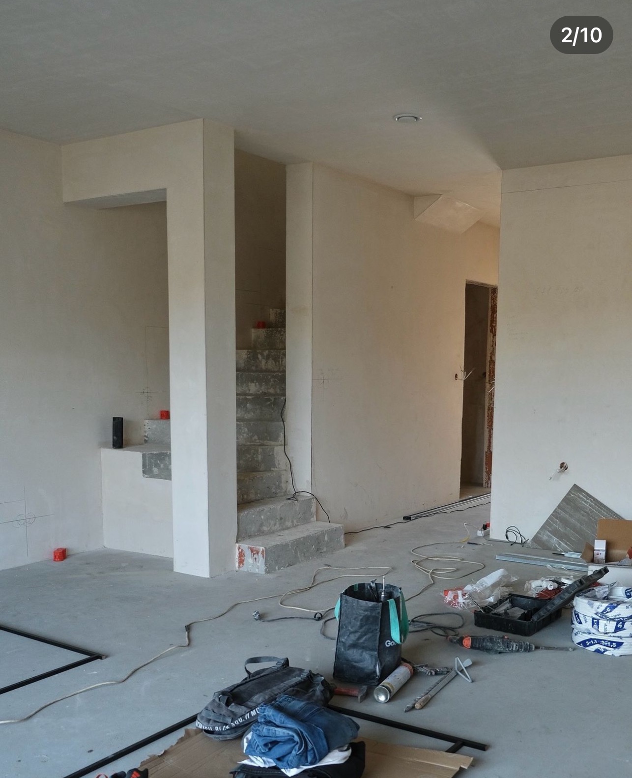 Surowe betonowe schody w surowym stanie, z widocznymi narzędziami i materiałami budowlanymi na podłodze w trakcie prac wykończeniowych.