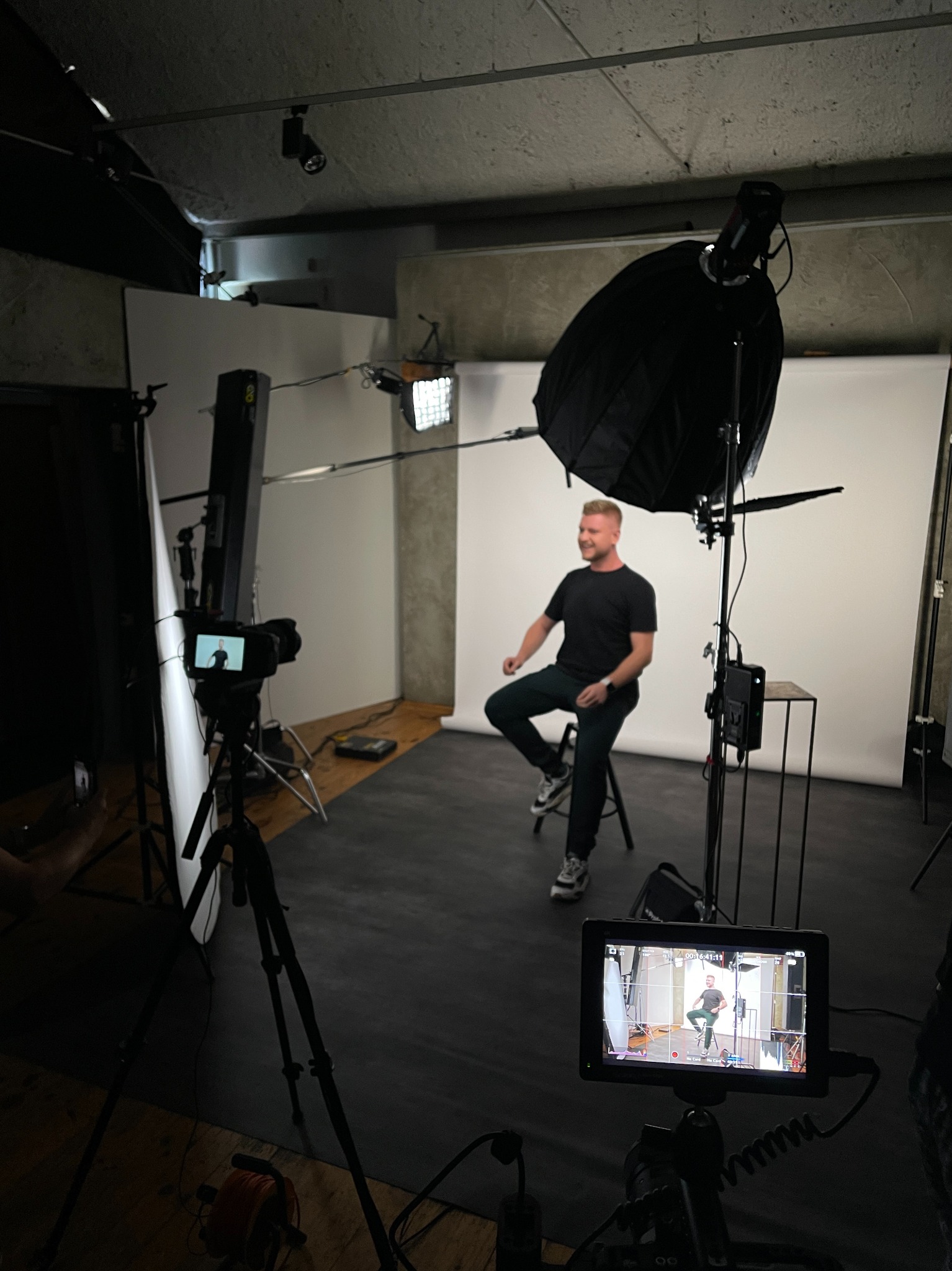 Ujęcie z planu filmowego w Warszawie: mężczyzna siedzi na krześle na tle białego ekranu, oświetlony lampami studyjnymi, widoczny na ekranie kamery.