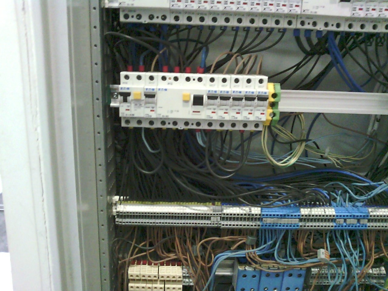 Otwarta szafa elektryczna z widocznymi bezpiecznikami Eaton, przewodami w różnych kolorach i listwami zaciskowymi.