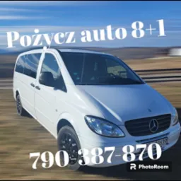 Biały Mercedes Vito z przyciemnianymi szybami i numerem telefonu nałożonym na obraz, jadący po drodze z rozmytym tłem krajobrazu.