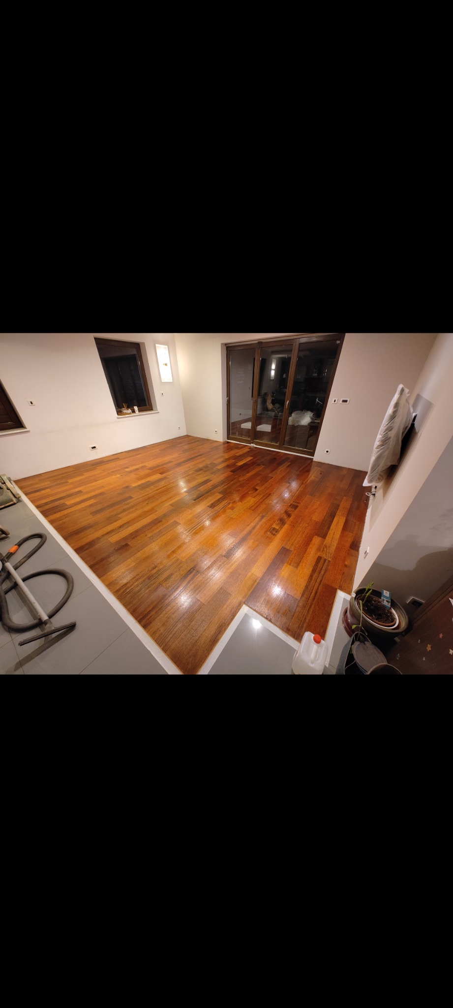 Błyszcząca, świeżo polakierowana podłoga z parkietu w pustym pokoju, widoczny odkurzacz przemysłowy i butelka z preparatem do pielęgnacji podłóg.