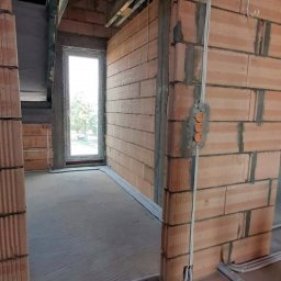 JB Energy Sp. z o.o. - Wnętrze w trakcie budowy z widoczną instalacją elektryczną: kable w peszlach biegnące po ścianach z cegły ceramicznej, puszki elektryczne pod tynk. Surowy stan wykończenia.